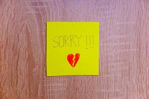 A heartfelt note on a yellow sticky note expresses deep remorse with a broken heart drawing. photo