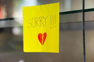 A heartfelt note on a yellow sticky note expresses deep remorse with a broken heart drawing. photo