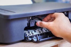 A person is installing a black ink cartridge into a printer. photo