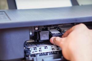 A person is installing a black ink cartridge into a printer. photo