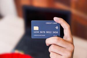 A person holds a credit card in front of a laptop, indicating online transactions. photo