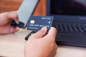 A person holding a credit card in one hand and a smartphone in the other while near a laptop. photo