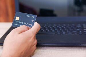 A person holds a credit card in front of a laptop, indicating online transactions. photo