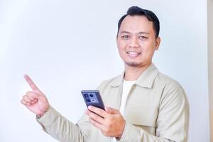 A man holding a smartphone, smiling and pointing upwards, conveying positivity. photo