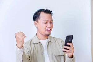 A surprised man expressing excitement and shock while hold smartphone and raised hands. photo
