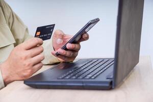 A person using a smartphone and credit card for online transactions at a laptop. photo