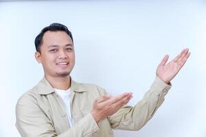 A young man in a beige jacket is smiling and gesturing with his hands in a welcoming manner. photo