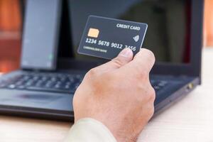 A person holds a credit card in front of a laptop, indicating online transactions. photo
