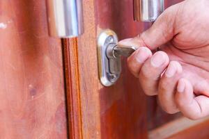A hand using a key to unlock a wooden door, symbolizing security and access. photo