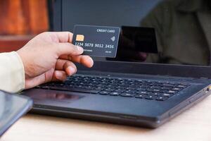 A person holds a credit card in front of a laptop, indicating online transactions. photo