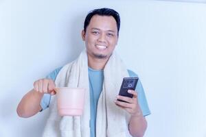 a smiling Asian man with a towel over his shoulder while holding his smartphone and a dipper photo