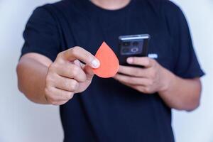 A person holds a red paper droplet while using a smartphone, symbolizing health awareness. photo