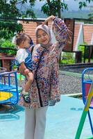 A Joyful young Asian muslim mom playing with her child at a vibrant playground under the sun. photo