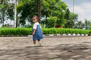 A beautiful Asian little child stands on a stone path surrounded by greenery photo