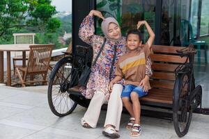 A asian mother wearing hijab and son share a joyful moment sitting on a bench. concept of mother's day photo