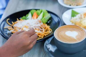 a portrait of a hand holding chopsticks to pick up pasta on a plate and a latte with a heart-shaped topping photo