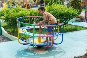A asian boy plays joyfully on a colorful merry-go-round in a sunny park, enjoying his childhood. photo