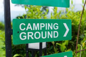 A green sign directing visitors to the camping ground, surrounded by greenery. photo