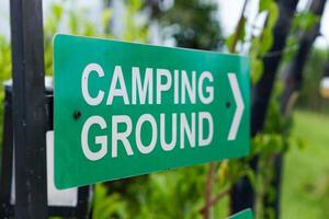 A green sign directing visitors to the camping ground, surrounded by greenery. photo