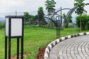 A modern lamp post stands in a lush green park, adding charm to the walking path around it. photo