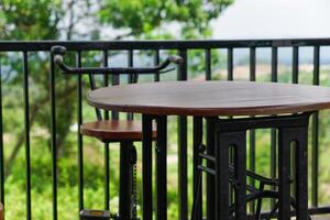 A wooden table and chair set on a balcony with a lush green view. photo