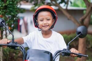 A happy asian boy in a bright helmet poses confidently on a electric scooter photo