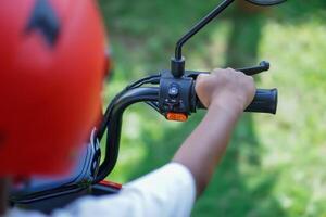 A child grips the handlebar of a bike, wearing a bright red helmet, ready to ride. photo