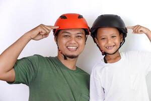A joyful asian father and son wearing helmets, pointing to their helmet, celebrating safety and fun together. photo