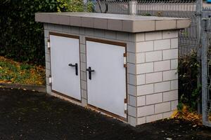A concrete utility storage unit with two white doors is placed in a photo