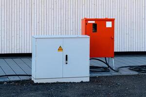 A white utility box and an orange control box near building photo
