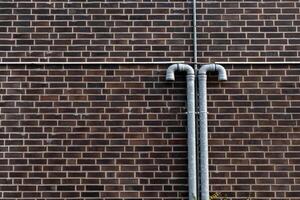 Two metal pipes extend vertically from a brick wall, showcasing a photo