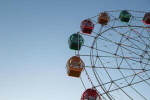 From below static ferris wheel against a clear blue sky, showcasing its symmetry and colorful patterns on the passenger cabins photo