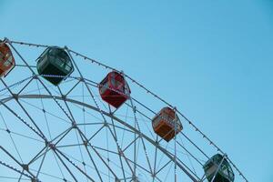 From below static ferris wheel against a clear blue sky, showcasing its symmetry and colorful patterns on the passenger cabins photo