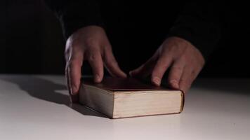 Man presenting an old Bible book on white table in the dark. Bible is suggested for finding answers video