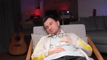 Man sleeping in armchair with remote control and glasses after watching tv video