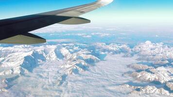 Passenger aircraft wing with snow-covered mountains. A scenic view of an airplane wing against snow-covered mountain peaks video