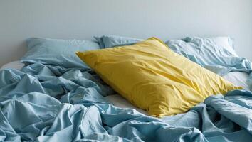A messy bed with a yellow pillow and blue sheets photo