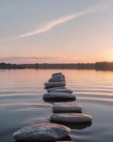 sereno puesta de sol terminado calma agua con apilado piedras reflejando ligero foto