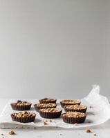Assorted chocolate tarts and crumble cups on baking paper and white surface photo