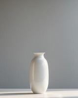 A white vase sitting on a table in front of a gray wall photo