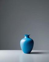 A blue vase sitting on a table in front of a gray wall photo