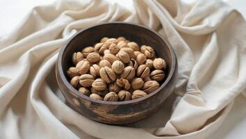 a wooden bowl filled with walnuts on a soft neutral fabric backdrop photo
