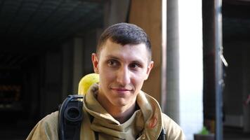 Portrait of confident male firefighter standing near fire station. Young fireman in protective uniform posing against the background of fire department. Concept of saving lives and heroic profession video