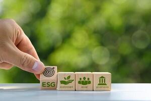 ESG concept of environmental, social and governance. Sustainable corporation development. A hand flips a wooden block with the abbreviation ESG onto the target icon. on a green background.. photo