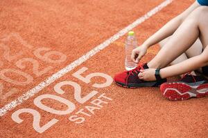 New year 2025 concept, beginning of success. Text 2025 written on asphalt road and male runner preparing for the new year. Concept of challenge or career path and change. photo