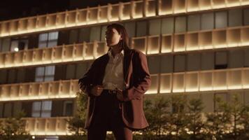Young ethnic woman in suit standing against illuminated building video