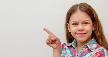 Smiling and happy child kid showing by index finger on copy space isolated on white background looking at camera waist up caucasian little girl of 7 years photo