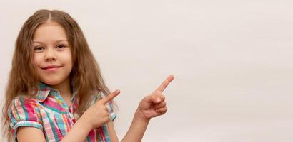 Smiling and happy little girl showing by index fingers on copy space photo
