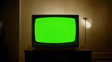 An old television with a green screen sits on a wooden cabinet in a dimly lit room. video