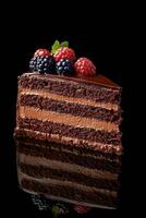 Chocolate cake slice with berries and mint against dark background photo